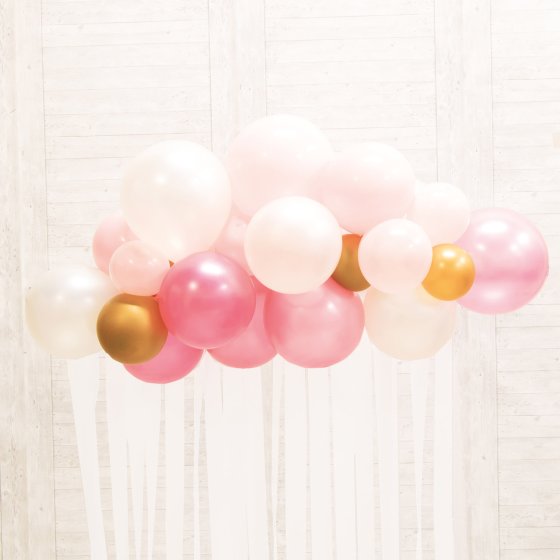 Balloon arch with pink, gold, and white balloons against a light background
